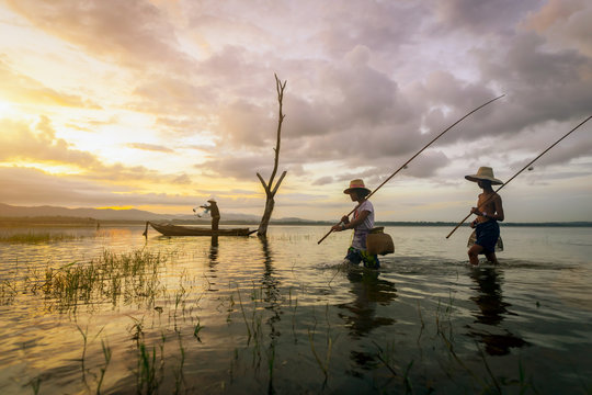 Asian boy and girl walking holding a fishing hook in the early morning. His uncle casting a net for catching freshwater fish on wooden boat in neighboring. Concepts nature and way of life.