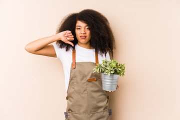 Young afro gardener woman holding a plant isolatedshowing a dislike gesture, thumbs down. Disagreement concept.