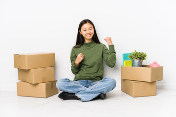 Young chinese woman moving to a new home raising fist after a victory, winner concept.