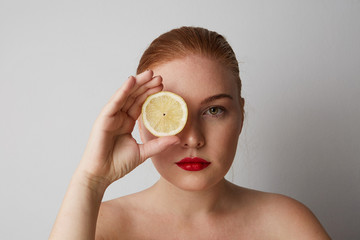 Close-up portrait of pretty young woman with red lips with closed eyes and holding a fresh lemon and posing on the gray wall. Isolated.