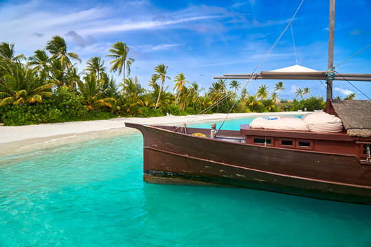Wooden ship on a white sand beach with palm trees and blue sky