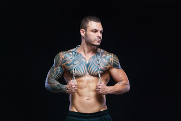 Fototapeta premium Tattooed strong muscular athletic man holding metal chain over his neck on black background