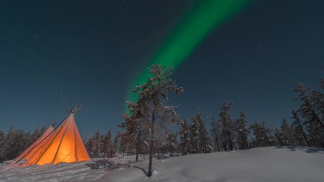 Aurora Borealis(northern lights) above teepee tent in snowy forest