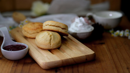 Cropped shot of scones on wooden tray with strawberry jam and clotted cream