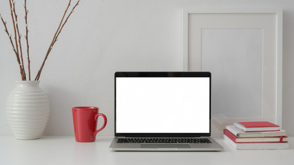 Close up view of stylish workplace with blank screen laptop, books, red mug and decorations on white table