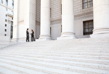 Two well dressed professionals in discussion on the exterior steps of a courthouse. Could be...