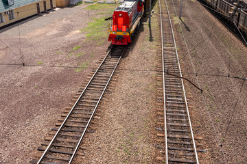 Red train on the railway tracks. Building, wagons, green grass. Top and front view. Concept of cargo transportation by rail.