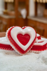 A red piece of handmade soap in the shape of a heart with a white insert, lying on a white towel against the background of wooden counters.