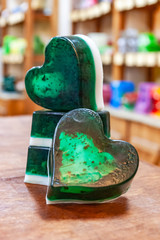 Four green pieces of handmade soap with white streaks stand on a wooden table against a background...