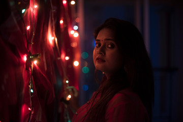 Portrait of an Indian Bengali beautiful brunette woman in front of the colorful light bokeh background created by tiny chain lights  in the evening of Diwali. Indian lifestyle and religion.