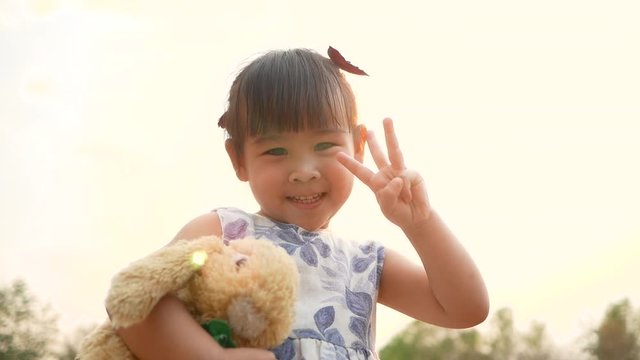 Cute Asian little girl hugging teddy bear with feeling love in public park.