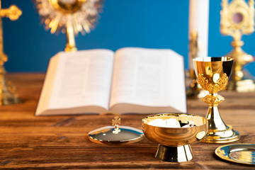 Catholic religion concept. Catholic symbols composition. The Cross, monstrance,  Holy Bible and golden chalice on the altar. Blue background.