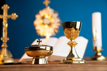Catholic religion concept. Catholic symbols composition. The Cross, monstrance,  Holy Bible and golden chalice on the altar. Blue background.