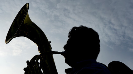 Silueta de músico tocando un instrumento musical o trompeta al atardecer