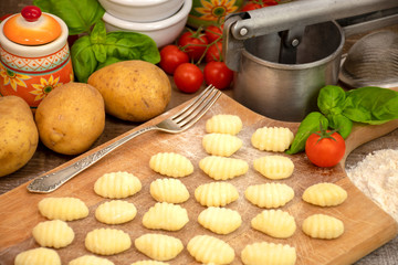 Uncooked homemade potato gnocchi on vintage cutting board over wooden table with flour, selective focus