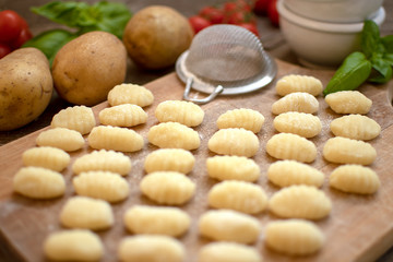 Uncooked homemade potato gnocchi on vintage cutting board over wooden table with flour, selective focus