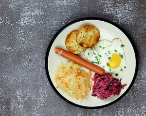 Fried eggs with sausage and sauerkraut in a white plate on a dark background. Top view, flat lay.