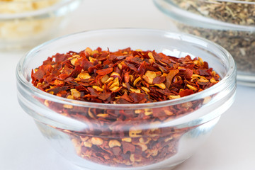 crushed red chili pepper in glass bowl.  Macro on white blurred background