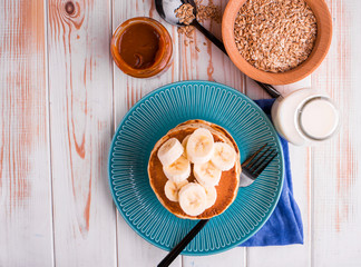 Useful and delicious breakfast with oatmeal, milk, tea, pancakes with banana and salted caramel.