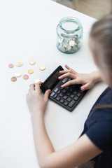Cute little child girl counts on a calculator and puts coins in a glass bottle in her room. The child saves money on the concept of the future