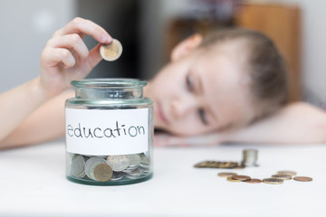 A little girl saves money for education. child counts and puts coins in a glass bottle in her room....