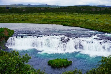 a picturesque small waterfall with turquoise water on the expanses of Iceland, a summer cloudy day