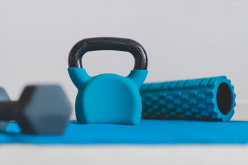 home gym concept, blue yoga mat with kettlebell foam roller and dumbbell shot at shallow depth of...