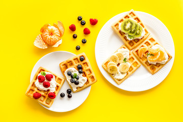 Fototapeta na wymiar Belgian waffles with creamy cheese and berries on yellow background top-down