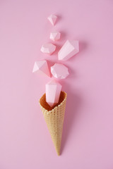 Hand holds a waffle cone with paper diamonds on pink background. Holiday concept.