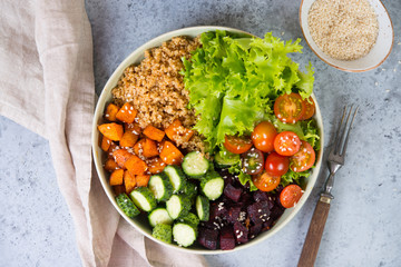 Vegetarian dish a bowl of healthy quinoa with fresh and baked vegetables on a gray concrete background. Close up, top view