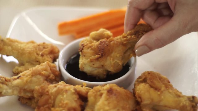 Female hand takes chicken leg and dips it in Teriaky sauce.