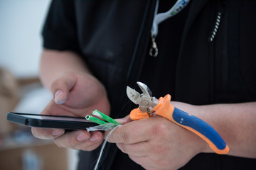 electrical engineer with wire and pliers in his hand using mobile phone