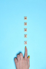 Top view woman hand pointing on women word spelled in wooden blocks on colorful blue background. Love, 8 march background. Gift, greeting, compliment concept. Copy space. place for text.