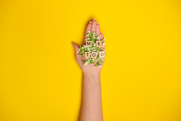 Phrase Me Too made of wooden letters in hand full of flowers on yellow background, top view. Stop sexual assault. Space left for text, copy