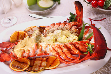 Baked lobster with applesauce and grilled bbq fruit on a white plate in a restaurant.