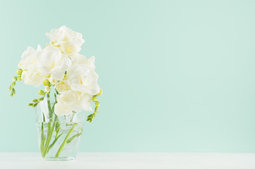 Spring gentle fresh flowers in transparent glass in elegant green mint menthe interior on white wood board, copy space.