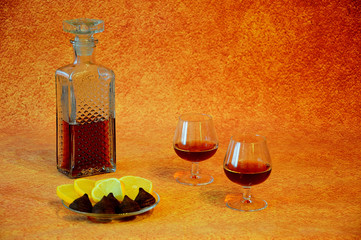 Crystal decanter with cognac and two glasses of drink next to a plate with appetizers, cut lemon...