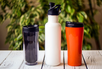 Assortment of refillable plastic and stainless steel water bottles on table against blurred...