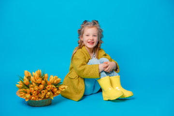 portrait of a child girl in a coat sitting and a bouquet of spring flowers on a colored blue background