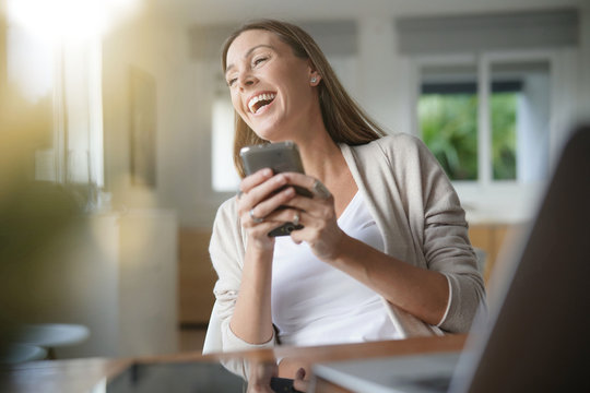 Cheerful woman at home using smartphone
