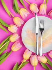 Easter table cutlery with tulips, feathers on pink background