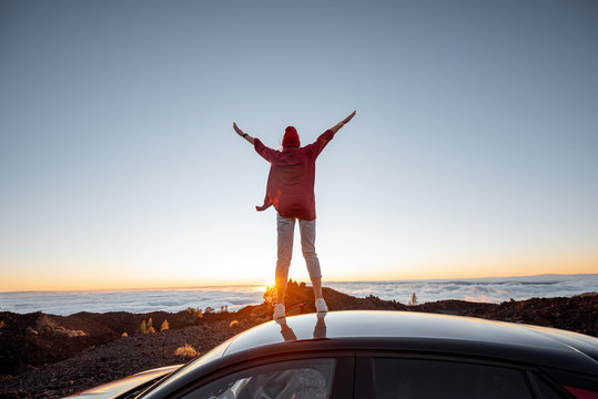 Woman enjoying rocky landscapes above the clouds on a sunset, standing on the car highly in the mountains. Carefree lifestyle and travel concept