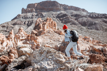 Young woman dressed casually in jeans with red hat and backpack hiking on the rocky terrain on a sunny day. Traveling on volcanic valley on Tenerife island