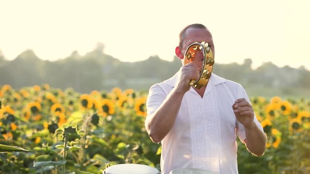 Happy dancer man playing tambourine and dancing energeticly in green summer field.
