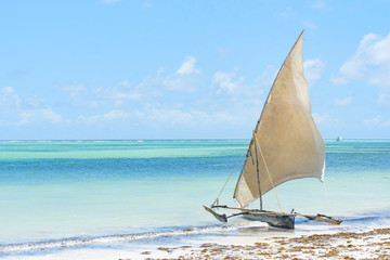 traditional African solid wood boats under sail on the shore of the Indian ocean with turquoise...