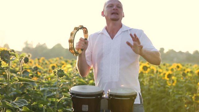 Happy dancer man playing tambourine and dancing energeticly in green summer field.