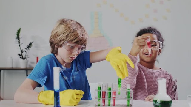 Blond Boy Interacting with Beautiful Dark-skinned Female Child in Science Classroom. They Looking on Test Tubes with Colour Liquid. Molecular experiment. Multiracial Kids Have Fun in School.
