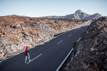 Landscape view on the volcanic valley with picturesque straight road and woman walking on it during a sunny day. Traveling on Tenerife island, Spain