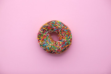Classic chocolate donut with colorful sprinkles on pink background. Sweet dessert for holiday...