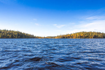 Blue sky and dark blue water of the forest lake on windy day